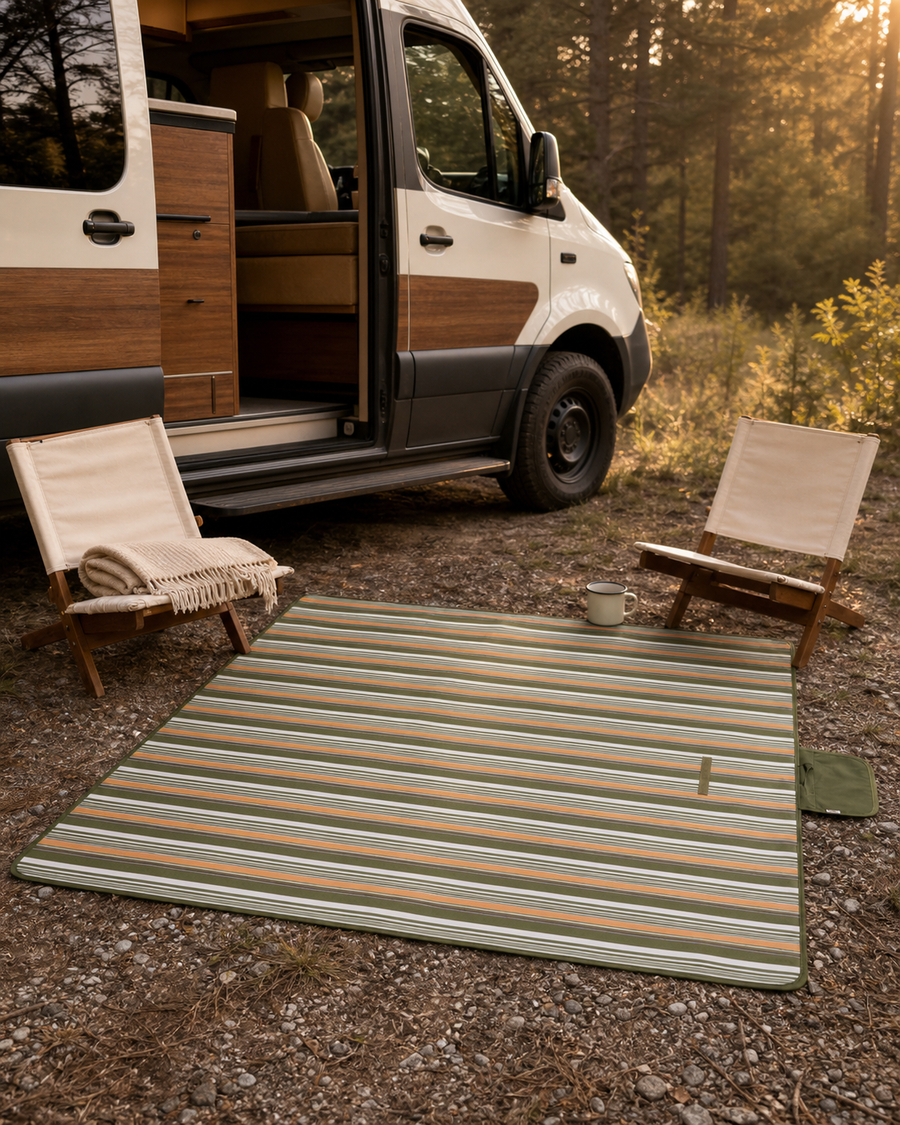 Forest, cream, and muted-orange striped camp mat beside a walnut-accented camper at golden hour